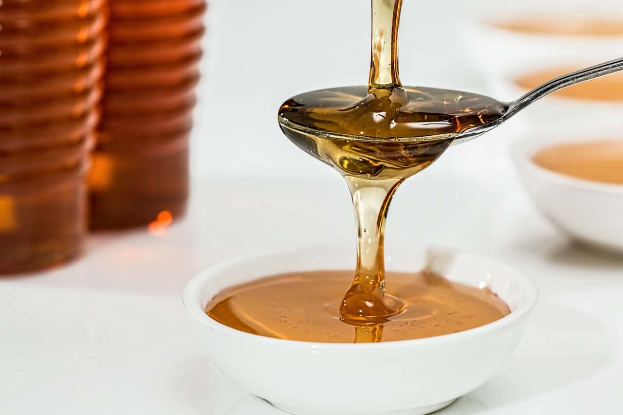 A spoonful of honey pouring into a cup